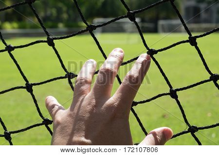 Man's hand extended to touch the mesh of a football field.