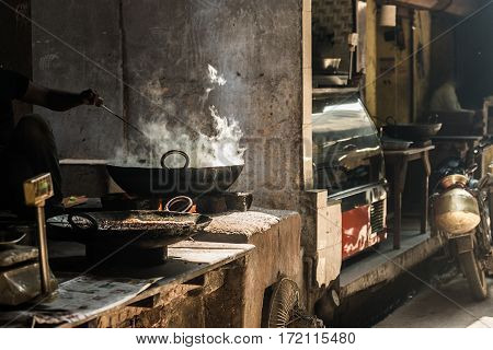 Unrecognizable Man Cooking In Fatiscent Big Pan Or Wok In A Small Street Food Stall. White Smoke Com