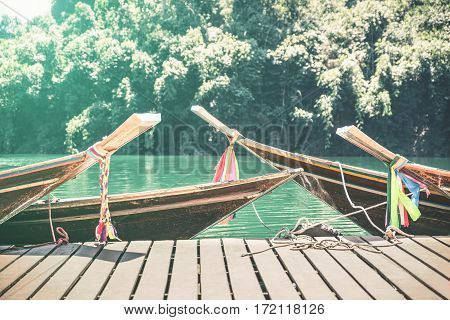 Longtail boats at Cheow Lan Lake on wooden jetty pier docks - Khao Sok national park in Thailand - Adventure travel concept with wanderlust feelings - Azure turquoise filter on sunflare halo sunshine