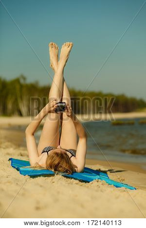 Summertime pleasures enjoying vacation concept. Woman in bikini sunbathing and relaxing on beach using smartphone checking social media and writing sms