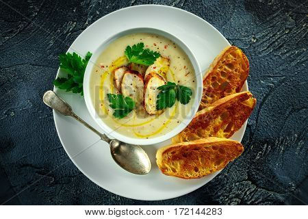 Creamy chicken soup with vegetables in bowl with chiabatta toast, parsley and nigela seeds sprinkle on stone table.