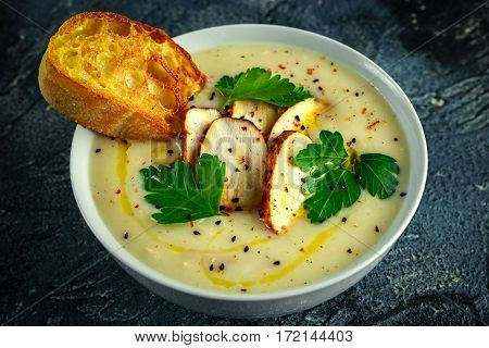 Creamy chicken soup with vegetables in bowl with chiabatta toast, parsley and nigela seeds sprinkle on stone table.