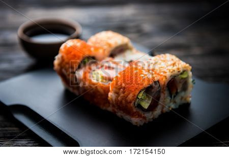close up of sushi rolls on black tray and dark wooden table
