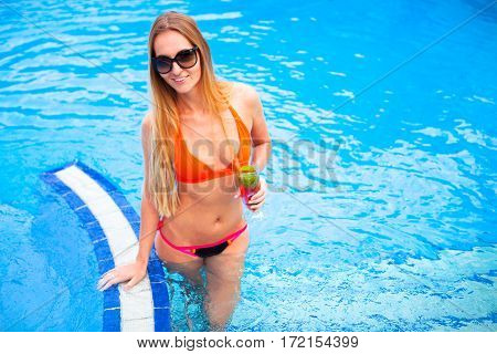 Young Pretty Blond Woman In A Orange Bikini And Sunglasses Enjoying Cocktail In A Swimming Pool