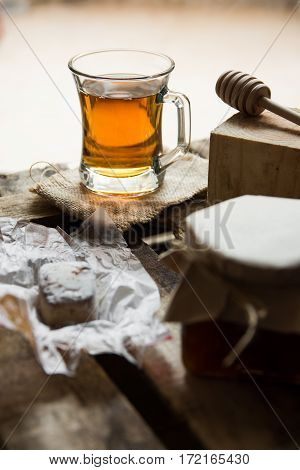 Glass cup with hot tea with jar of honey or jam wood spoon Spanish cookie polvoron on vintage box rustic vintage interiorcozy atmosphere