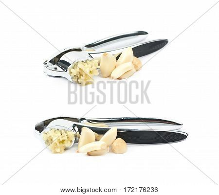 Metal garlic press utensil next to a pile of fresh cloves isolated over the white background, set of two different foreshortenings