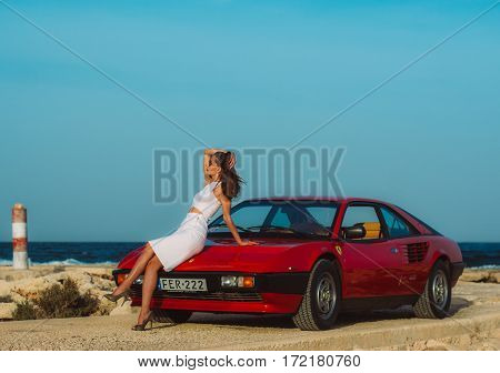 Young Beautiful Girl In Sunglasses Sitting On The Hood Of The Red Ferrari