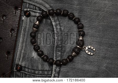 Bracelet on a hand of black stone. Clothing and accessories. black jeans with a leather belt close-up.