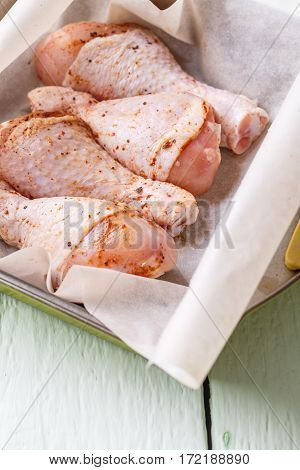 Uncooked chicken drumsticks on plate on white wooden table