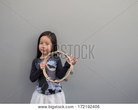 Little Asian Child Play The Tambourine, Gray Background