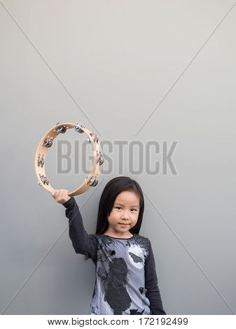 Little Asian Child Play The Tambourine, Gray Background