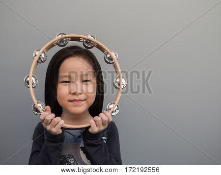 Little Asian Child Play The Tambourine, Gray Background