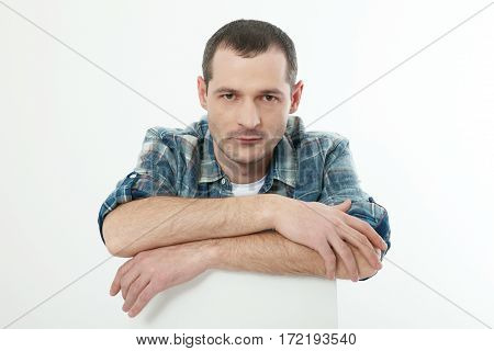 Portrait of smart serious young man in shirt sitting against white background