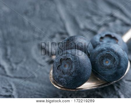Freshly picked blueberries in spoon closeup. Ripe and juicy fresh blueberries on textured concrete background. Bilberry on dark background with copyspace. Blueberry antioxidant. Healthy eating concept