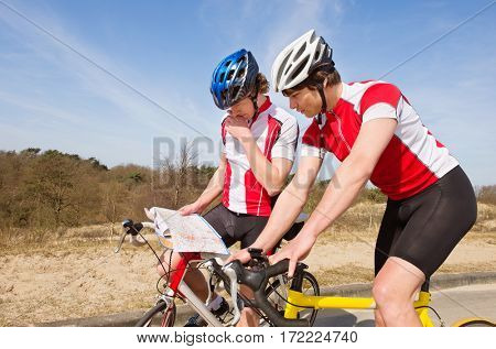Two lost cyclists looking for a map for directions, standing over their bicycles