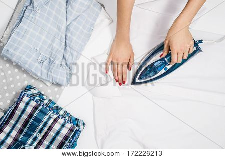 Female hand ironing clothes top view isolated on white background. Young woman with iron ironing man's shirt seen from above during housework. Blue iron on white table.
