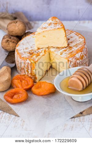 Soft cheese with cut off slice creamy texture orange rind with mold French German Alps honey dipper walnuts dried apricots knife top view rustic kitchen interior