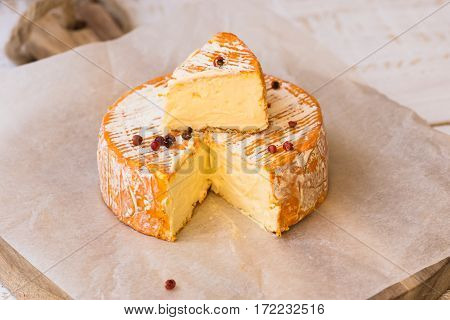 Top view of cut slice of French or German soft cheese with orange rind with mold creamy texture red pepper corns waxed paper wood cutting board