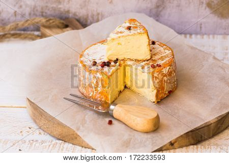 Top view of cut slice of French or German soft cheese with orange rind with mold creamy texture red pepper corns waxed paper fork wood cutting board