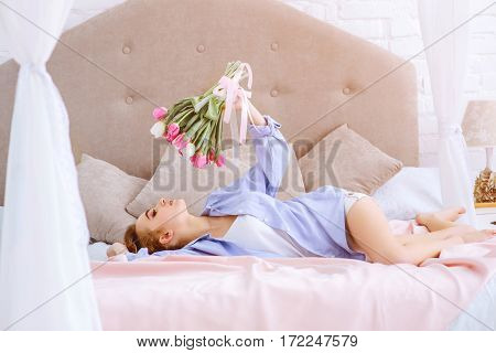 portrait of pretty woman with flowers lying on the bed in the morning