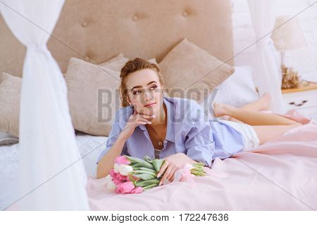 beautiful young girl with bouquet of pink and white tulips lying on the bed