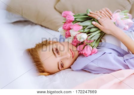 beautiful young girl with bouquet of pink and white tulips lying on the bed