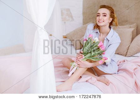 beautiful woman with white and pink tulips smiling on the bed