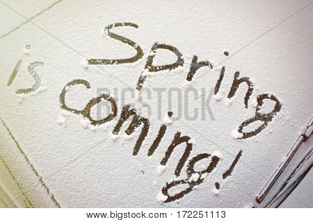 the inscription on the snow-covered car windshield spring is coming.