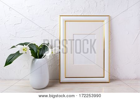 Gold decorated frame mockup with tender white lily in vase. Empty frame mock up for presentation artwork.