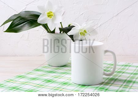 White mug mockup with lily in vase on green checkered napkin. Empty mug mock up for design promotion.