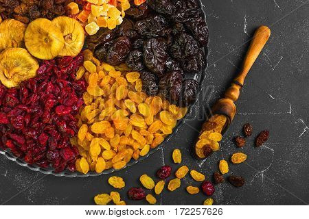 Assortment of dried fruit and candied fruit. Fruits figs prunes raisins papaya pineapple cranberries are laid out in rows on black background in the glass dish. Dry fruits in measuring spoon.