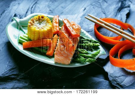 Salmon steak grilled with peppers and aspargus on a black stone background.