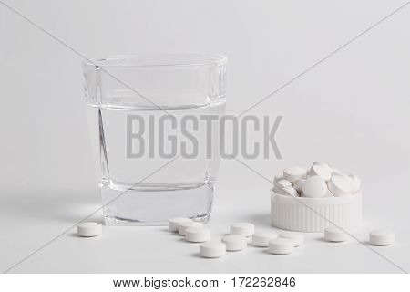 Round white pills and glass of water on a table waiting for eat