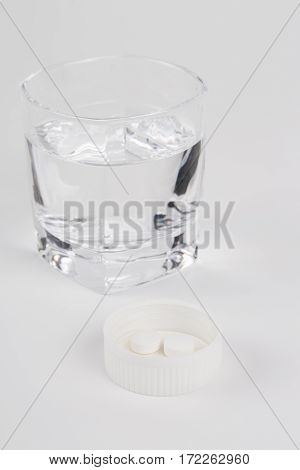 Round white pills and glass of water on a table waiting for eat