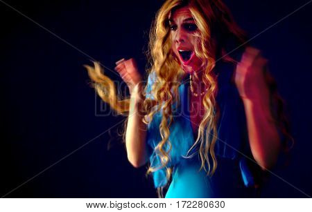 Frightened woman screaming with fear indoor at halloween night. Horror. Girl with tousled hair bawl covers her mouth with her hands black background.