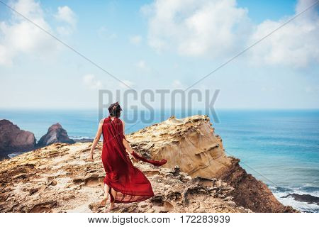 Girl in red dress among rocks and cliffs along the Coast of Algarve.