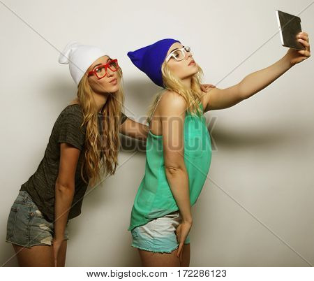 two hipster girls friends taking selfie with digital tablet, studio shot over gray vackground