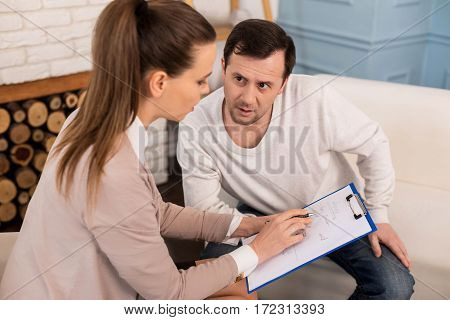 What is it with me. Nice thoughtful handsome man sitting on the sofa and looking at the therapist while listening to his diagnosis