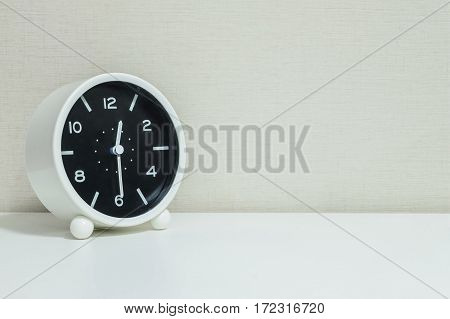 Closeup black and white alarm clock for decorate show show half past twelve or 12:30 a.m. on white wood desk and cream wallpaper textured background with copy space