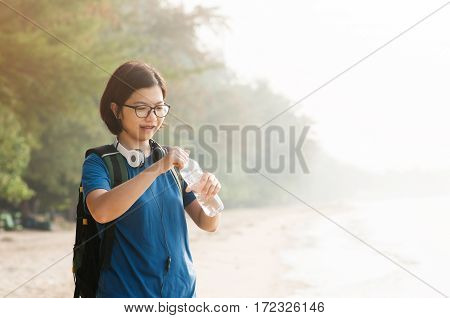 Asian woman traveller holding bottle of water for drink after on sea background.