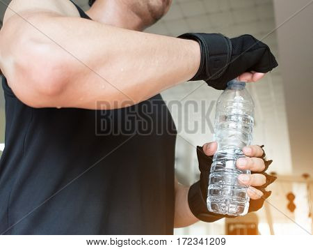 Close up man hands wear gloves opening bottle of water at a gym. Tired thirstily.