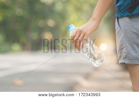 Asian woman hitchhiker hand holding bottle of water on nature background. copy space. Traveler.