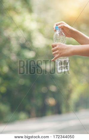 Close up Asian woman hand holding bottle of water on nature background. copy space. Traveler.