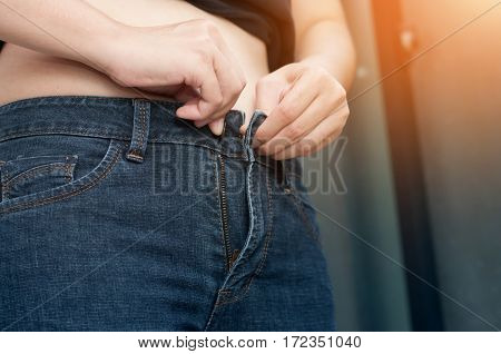 Close up woman hands with belly fat unable to close jean pant.