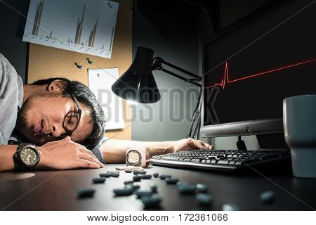 Asian man wear eyeglasses be ill and having heart attack. Pills spilling out of pill bottle foreground. Feeling tired exhausted unconscious overworked. Asian designer wear eyeglasses fall asleep.