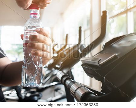 Close up fat man hands opening bottle of water on exercise bike cycling stationary exercising. Tired.