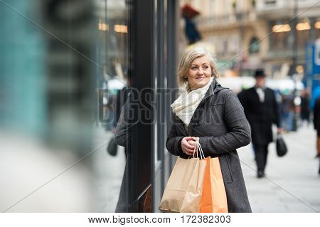 Beautiful senior woman in black coat and woolen scarf window shopping in historical centre of the city of Vienna, Austria. Winter.