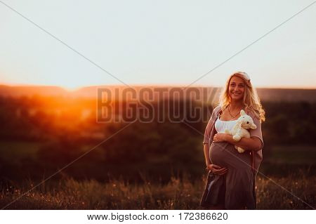 the pregnant girl with a hat in the field of wheat on a sunset