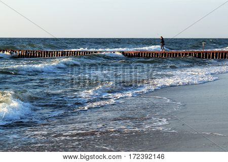 An unknown young woman walking along the old german breakwater toward to the Baltic Sea.