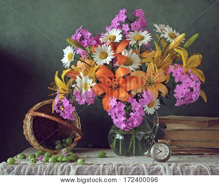 summer bouquet of lilies daisies and Phlox in the jar and gooseberries on the table.